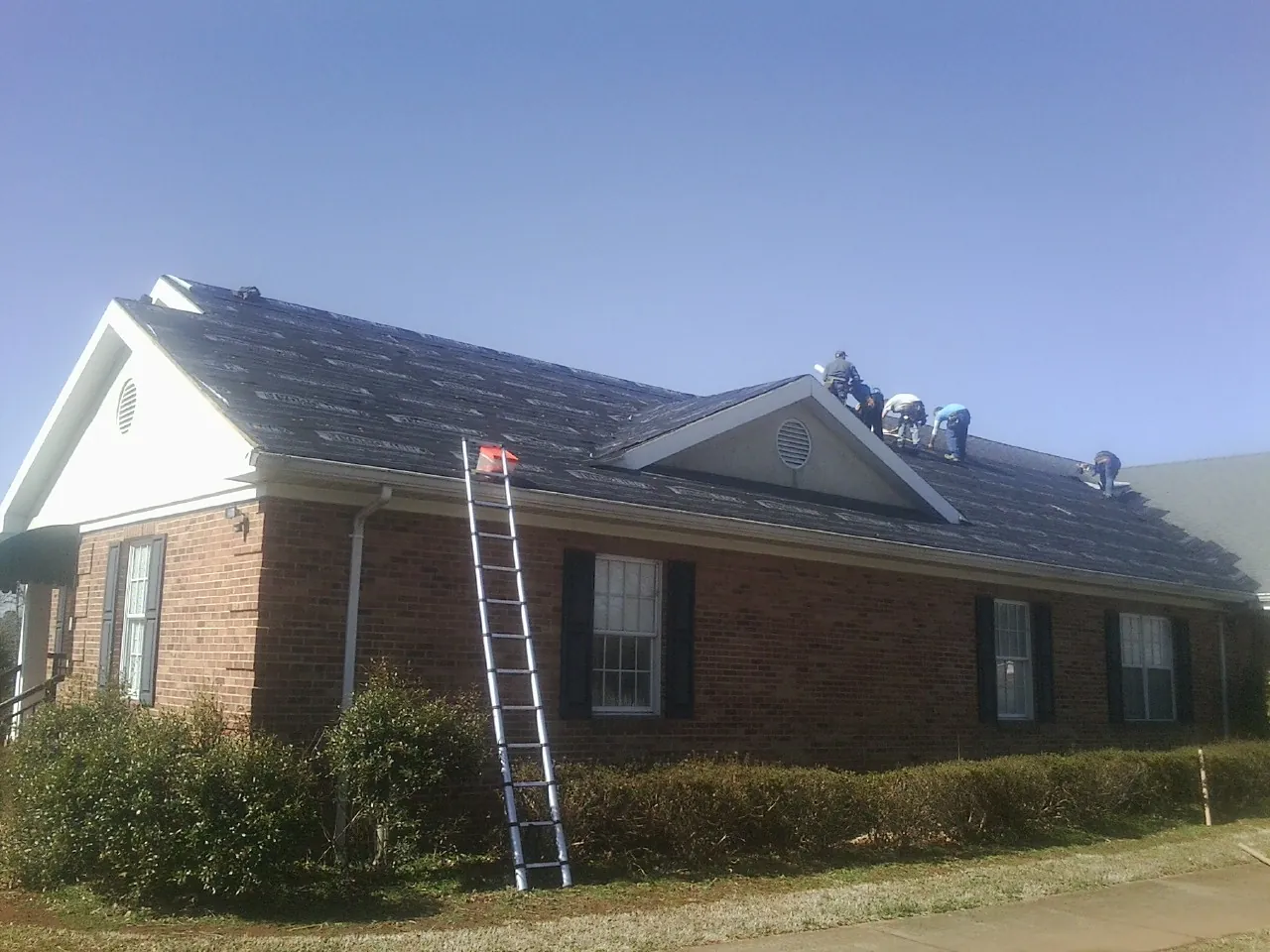 Crew tearing shingles off a brick ranch roof with a ladder set — Emergency Roof Repair work by our crew in Obernburg