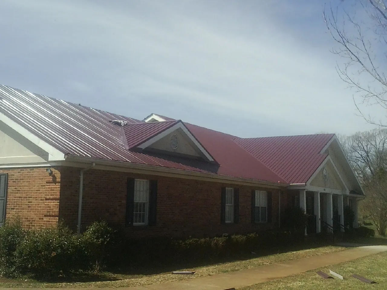 Red metal roof with gabled entries on a long brick building, from a Hail Damage Roof Repair job in Obernburg