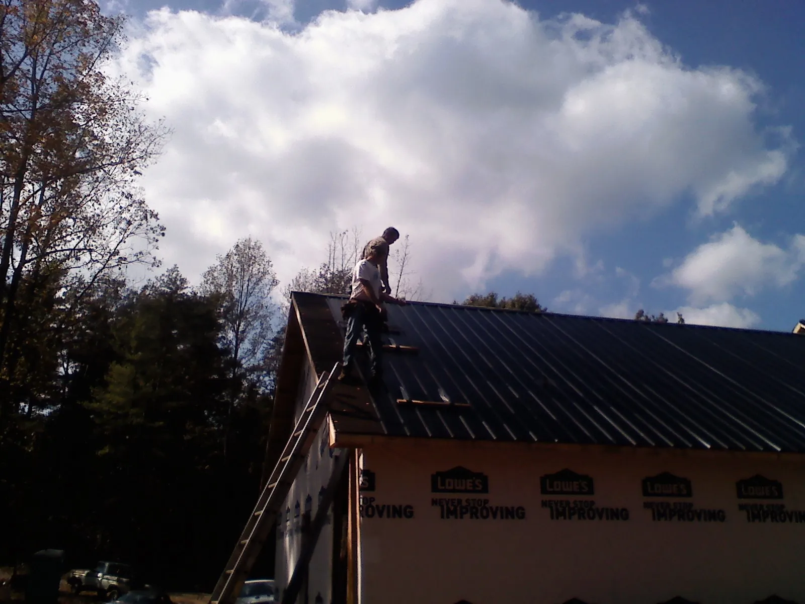 Roofer fastening dark metal panels high against a cloudy sky, from a Roof Inspection job in Obernburg