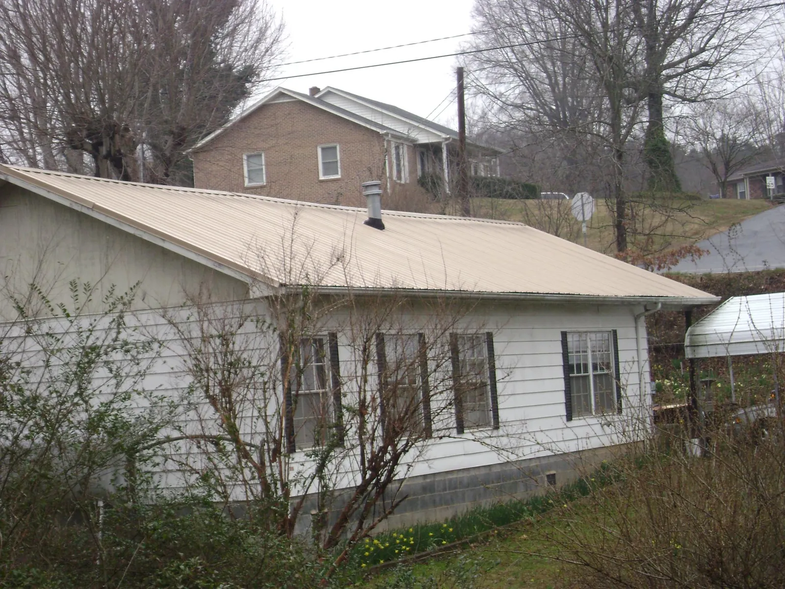 Tan metal roof on a white sided house set into a hillside — Commercial Roofing by Roofing Brothers in Obernburg